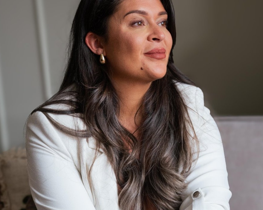 Christina, eigenaar van Elitehouse, in een witte blazer bij het raam van de salon